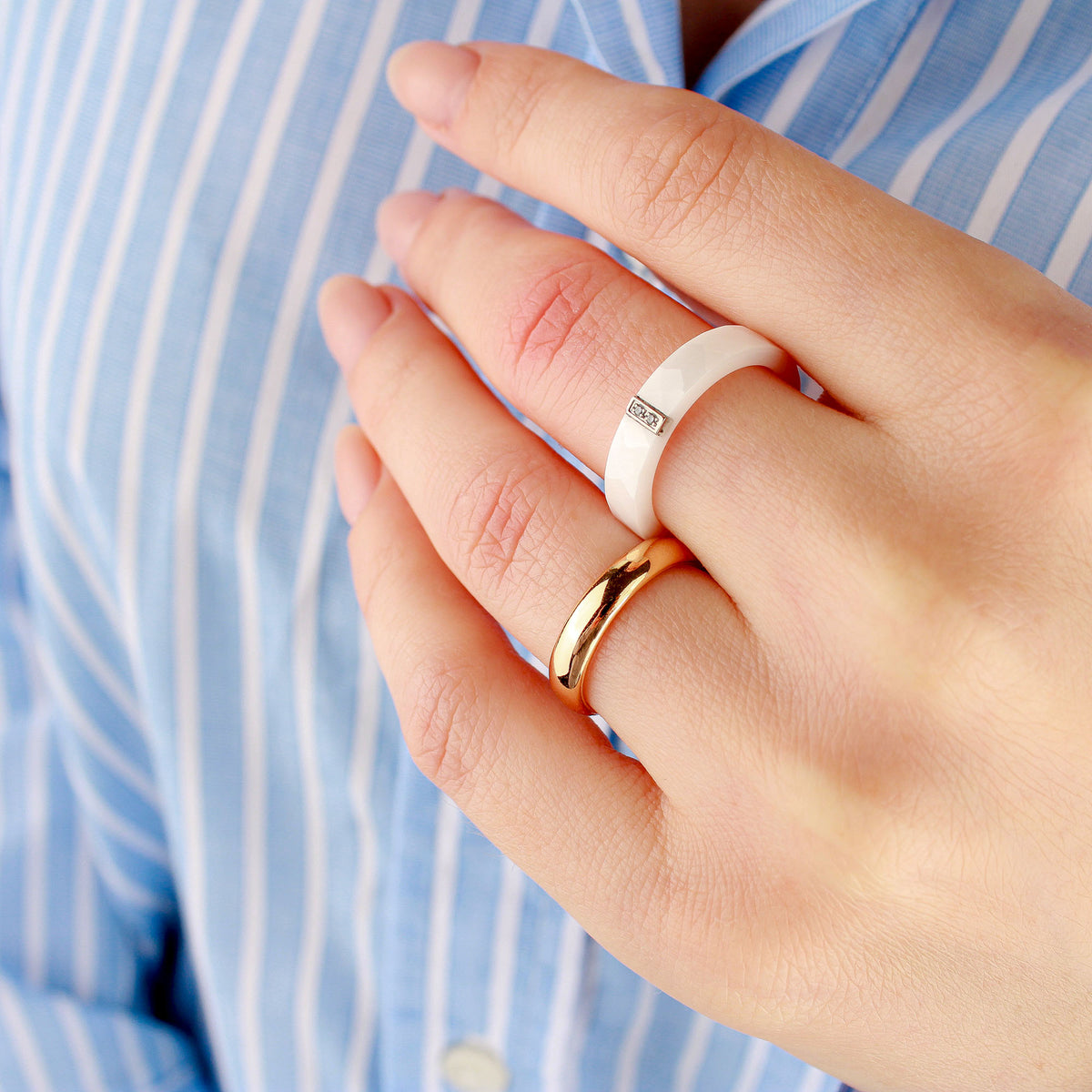 Smooth gold-plated wedding band on a woman's hand next to a white ceramic ring