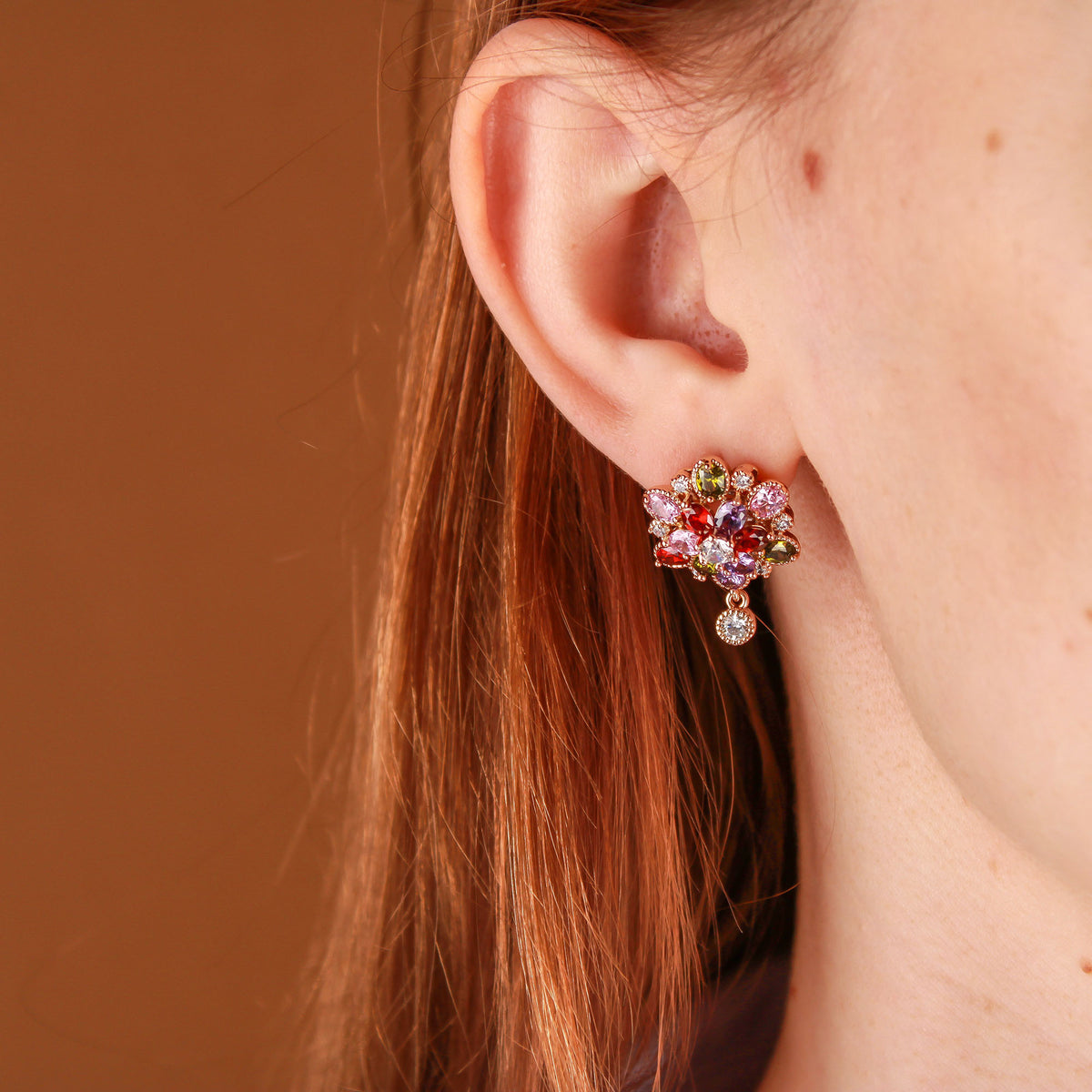 Flower earring with colourful stones on a model, a clear stone sparkling below