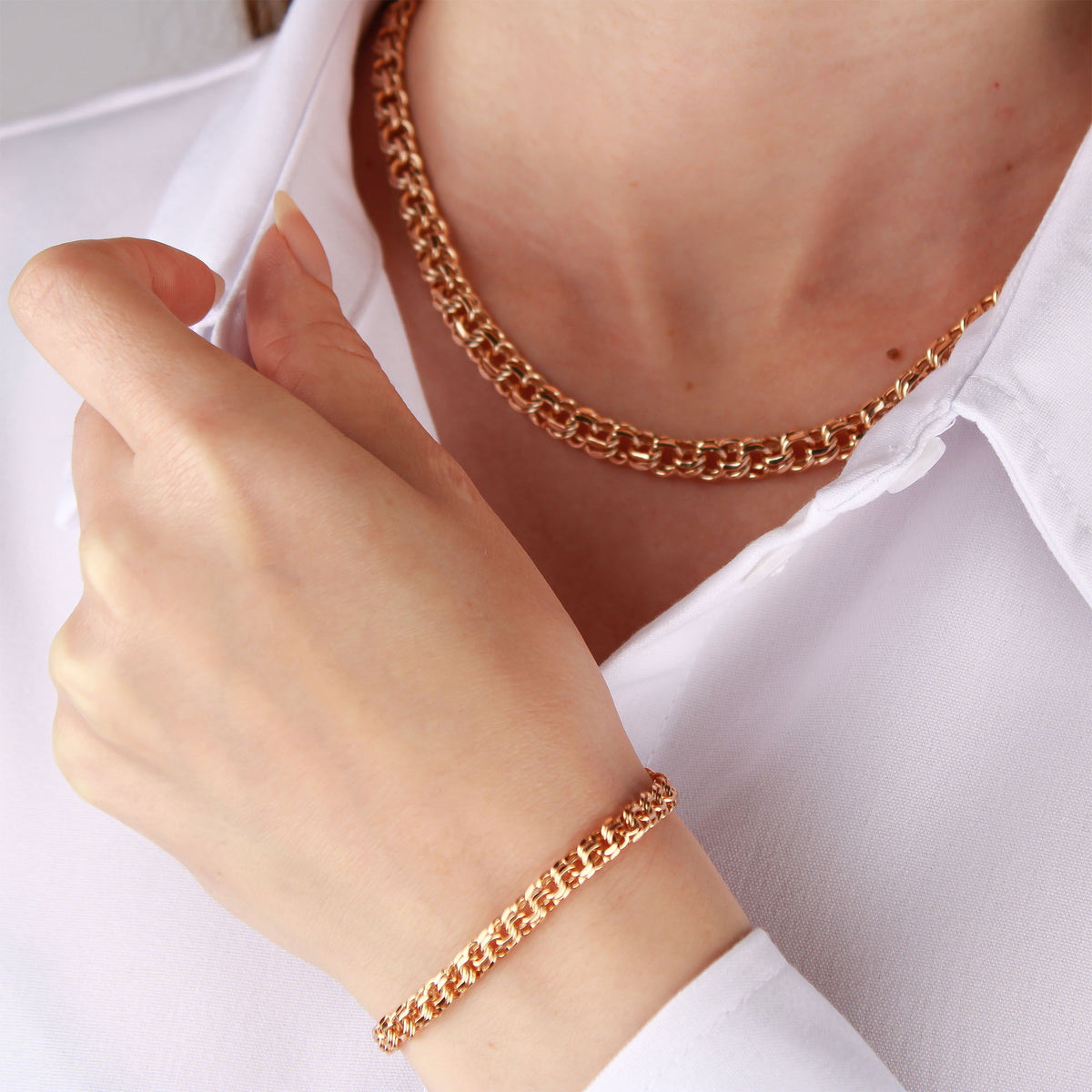 Woman in a white shirt wearing a chunky reddish gold-tone chain and matching bracelet