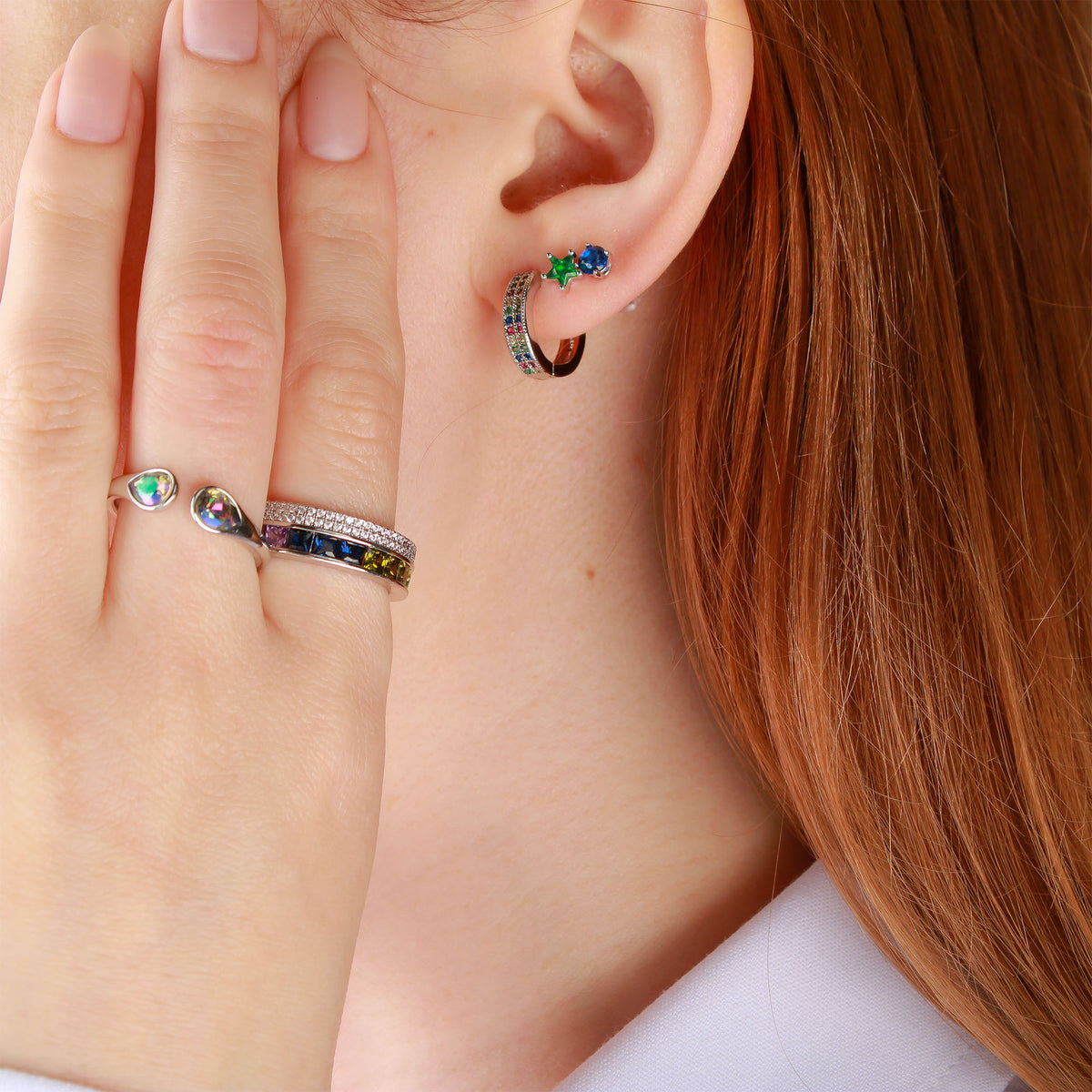 Green star stud earring on a model's ear beside a coloured crystal hoop