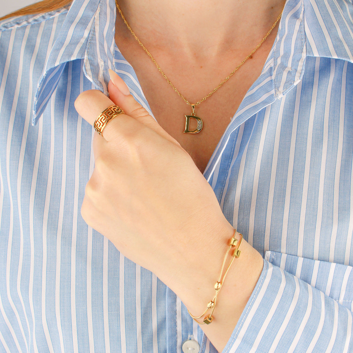 Gold-tone bracelet on a model's wrist beside a light blue striped blouse