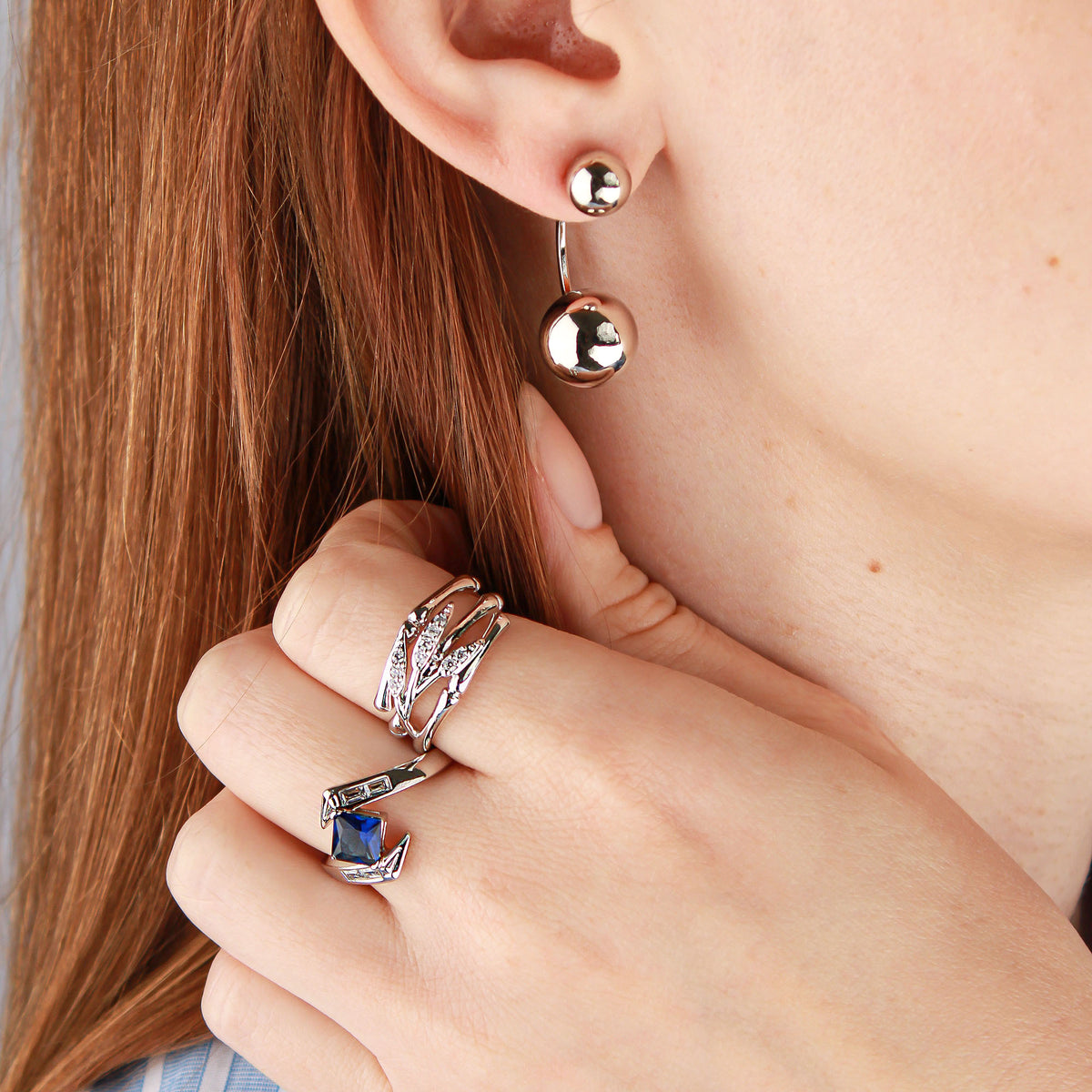 Model wearing silver-tone ball earrings, with rings on her fingers