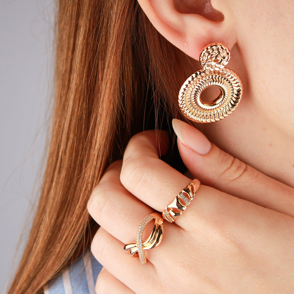 Model wearing the gold-plated infinity ring with patterned earrings and another ring