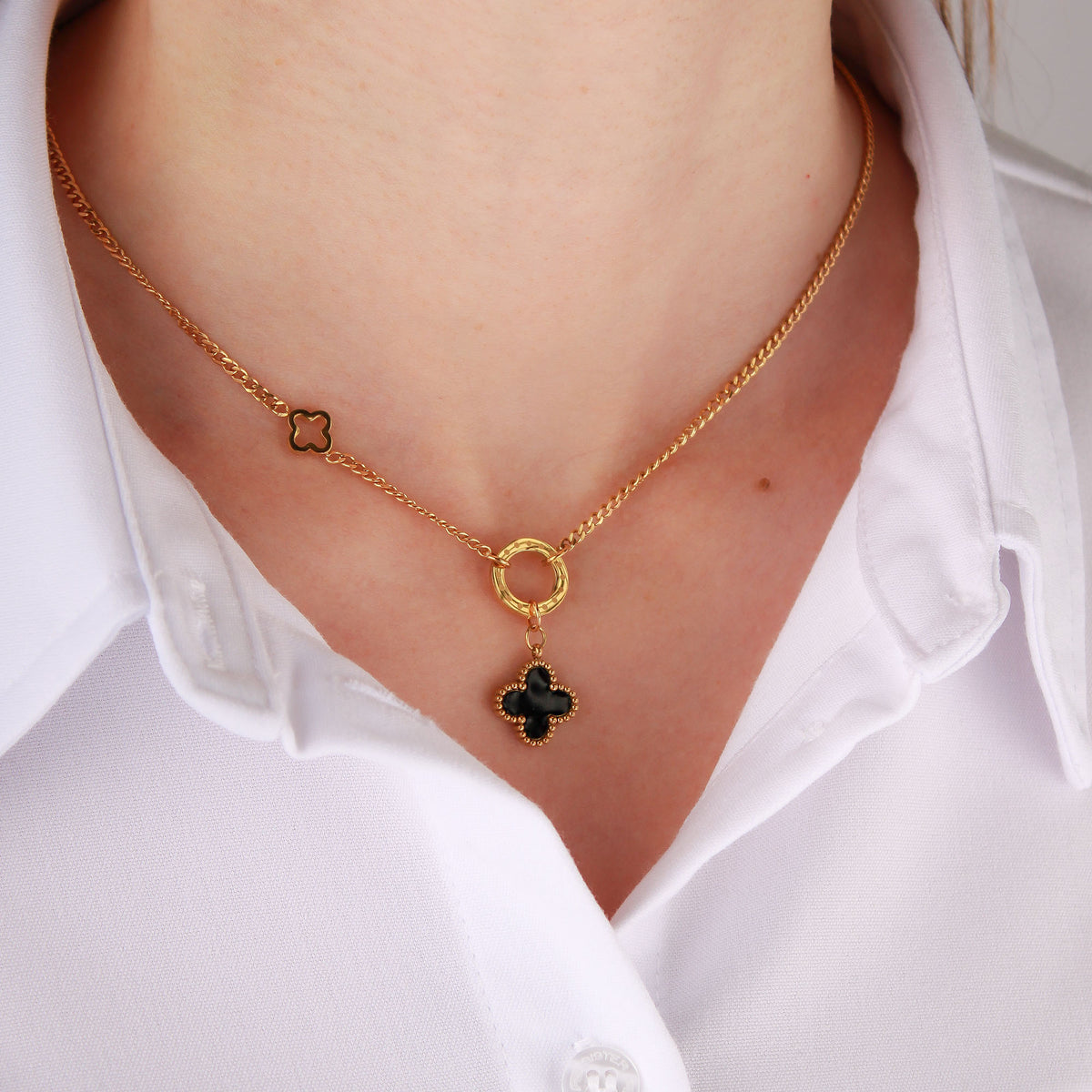Gold-plated necklace with a black four-leaf clover worn over a white shirt