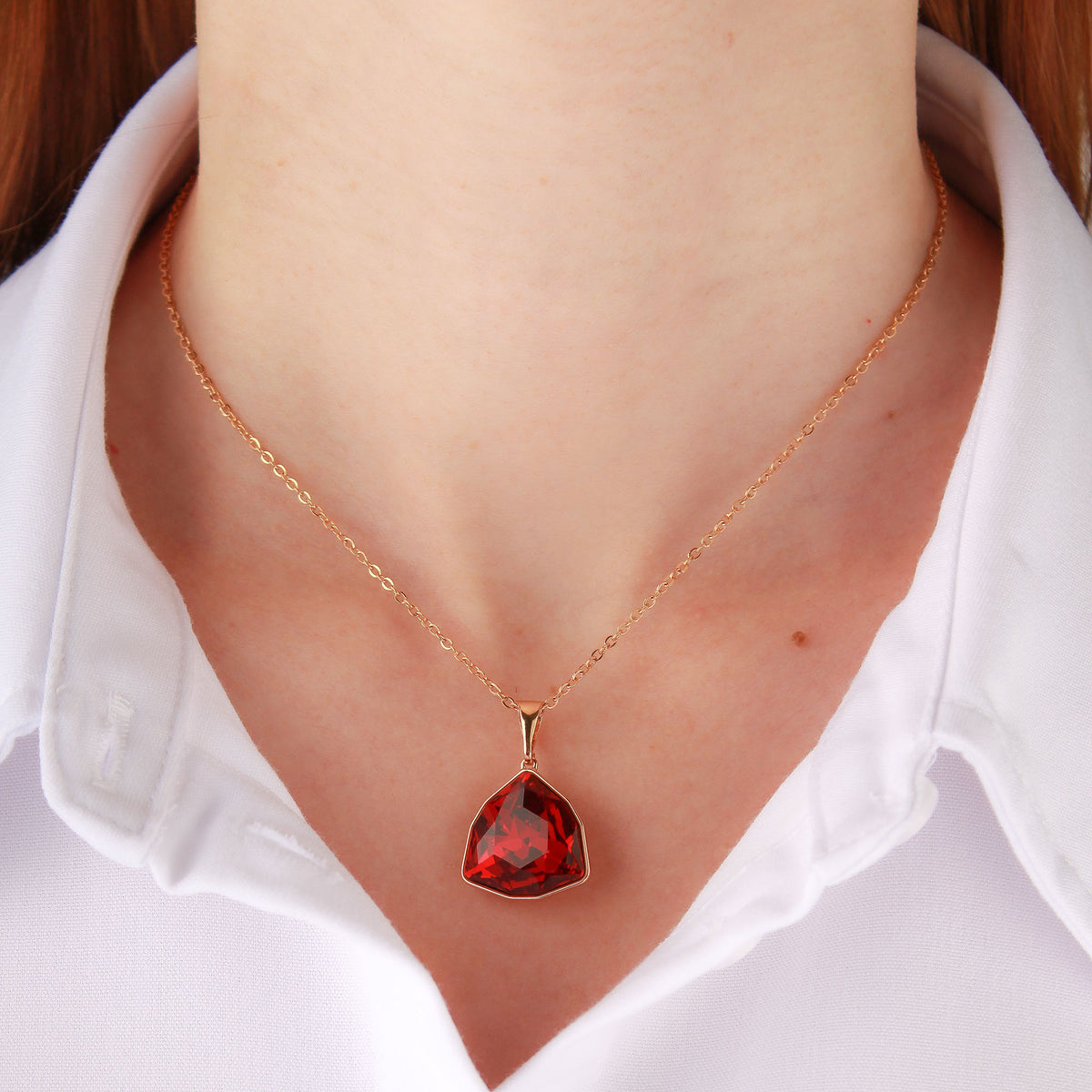 Woman in a white shirt wearing a gold-plated necklace with a red triangle pendant