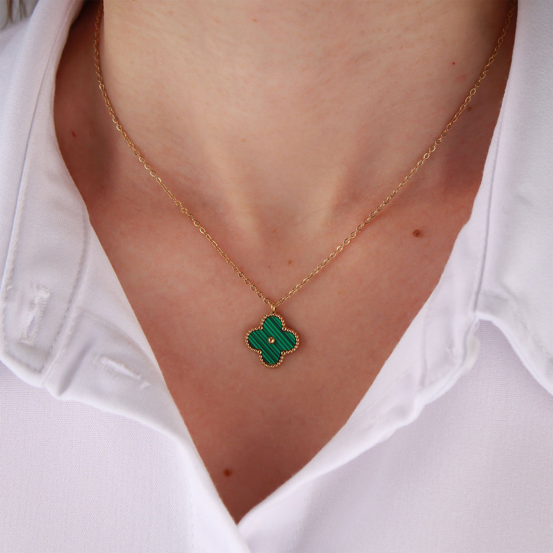 Model in a white shirt wearing a green four-leaf pendant on a gold-tone chain
