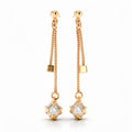 Long gold-tone earrings with two chains, a cube and a square-set clear stone