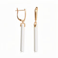 Long earrings with white ceramic cylinders and gold-tone leverback clasps on white