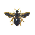 Bee brooch with a gold-plated body and black crystals in the wings, white background
